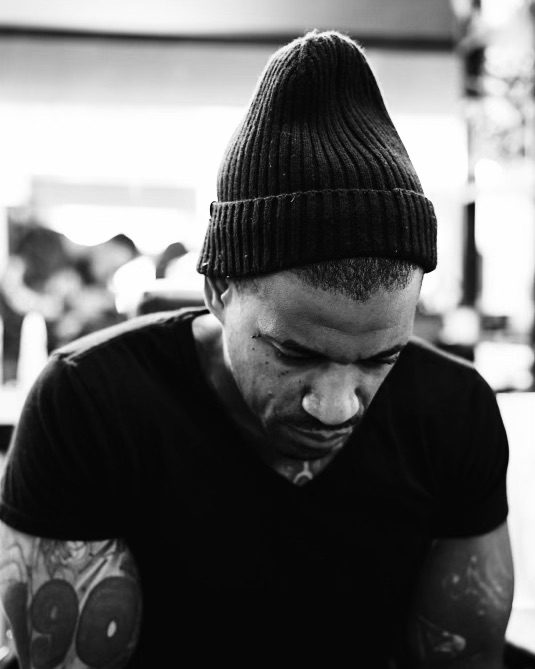 Black-and-white portrait of the founder in a knit beanie and dark T-shirt, looking down at his phone.